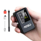 RoosCamp Air Master LT Bike Pump held in one hand showing LCD display, with Presta and Schrader valve adapters and needle attachment alongside