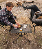 Couple at campsite using RoosCamp Portable Camping Table with food, drink and book on the surface, viewed from above