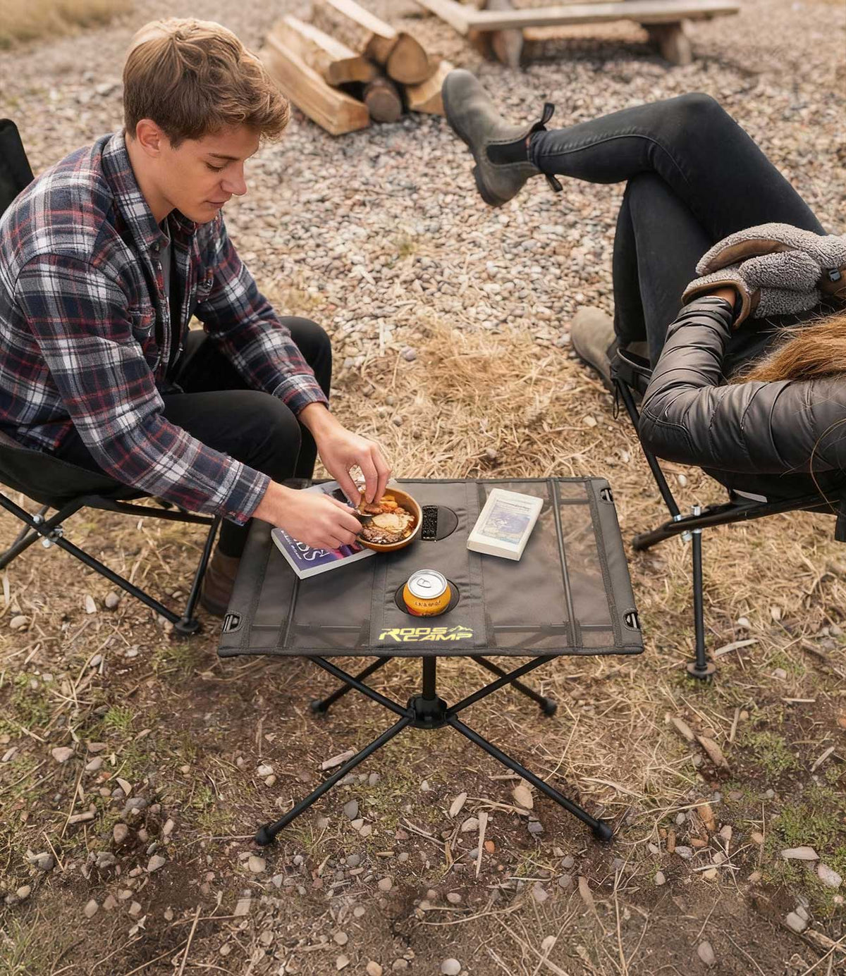 Couple at campsite using RoosCamp Portable Camping Table with food, drink and book on the surface, viewed from above