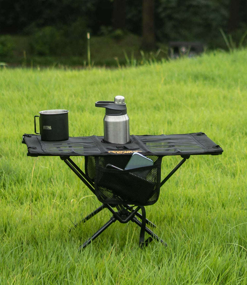 RoosCamp Portable Camping Table on grass with camping mug, flask and phone in side mesh pocket