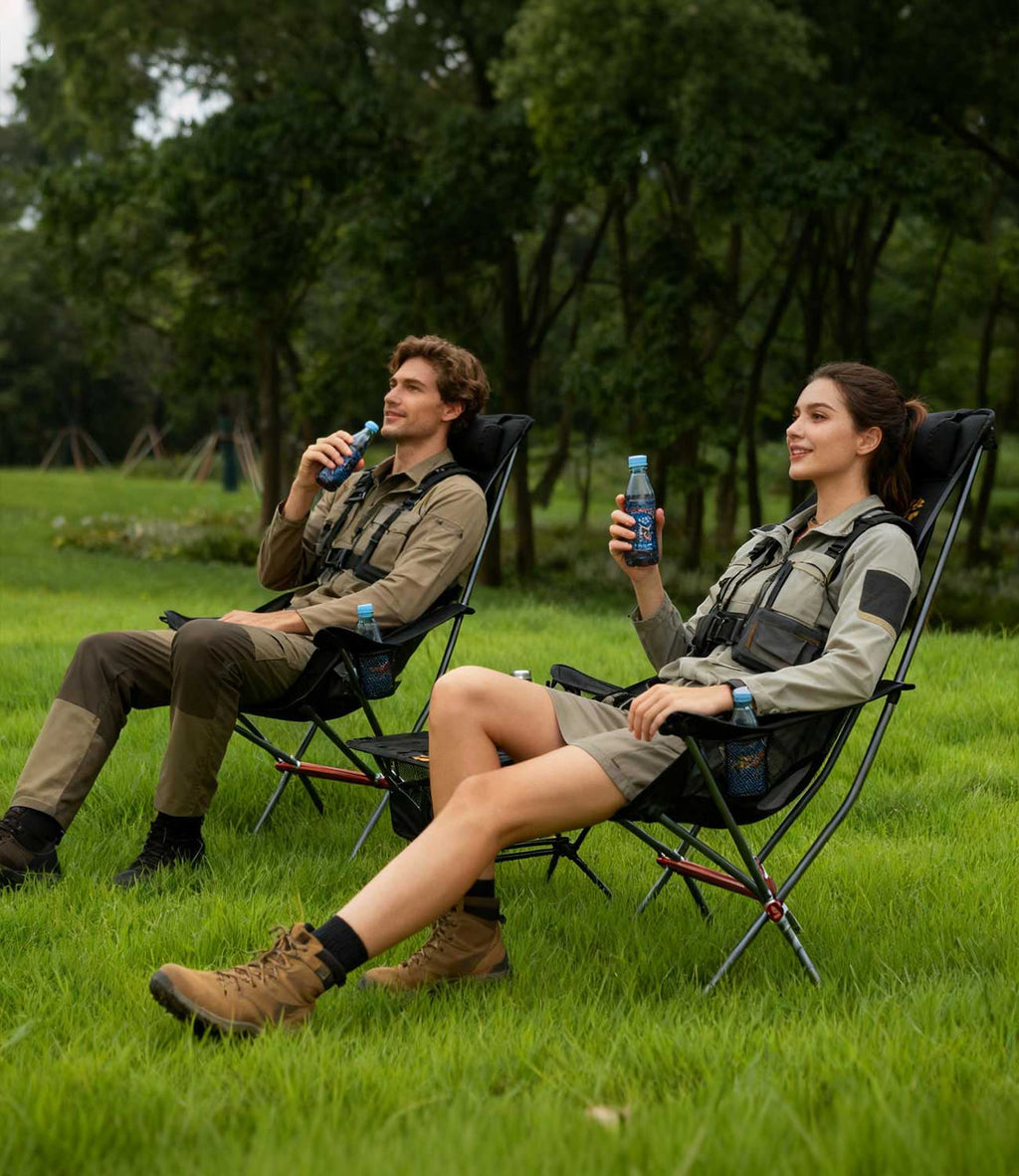 Two people in outdoor gear relaxing in RoosCamp High-Back Camping Armchairs on grass