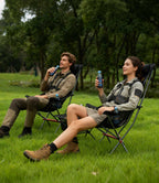 Two people in outdoor gear relaxing in RoosCamp High-Back Camping Armchairs on grass