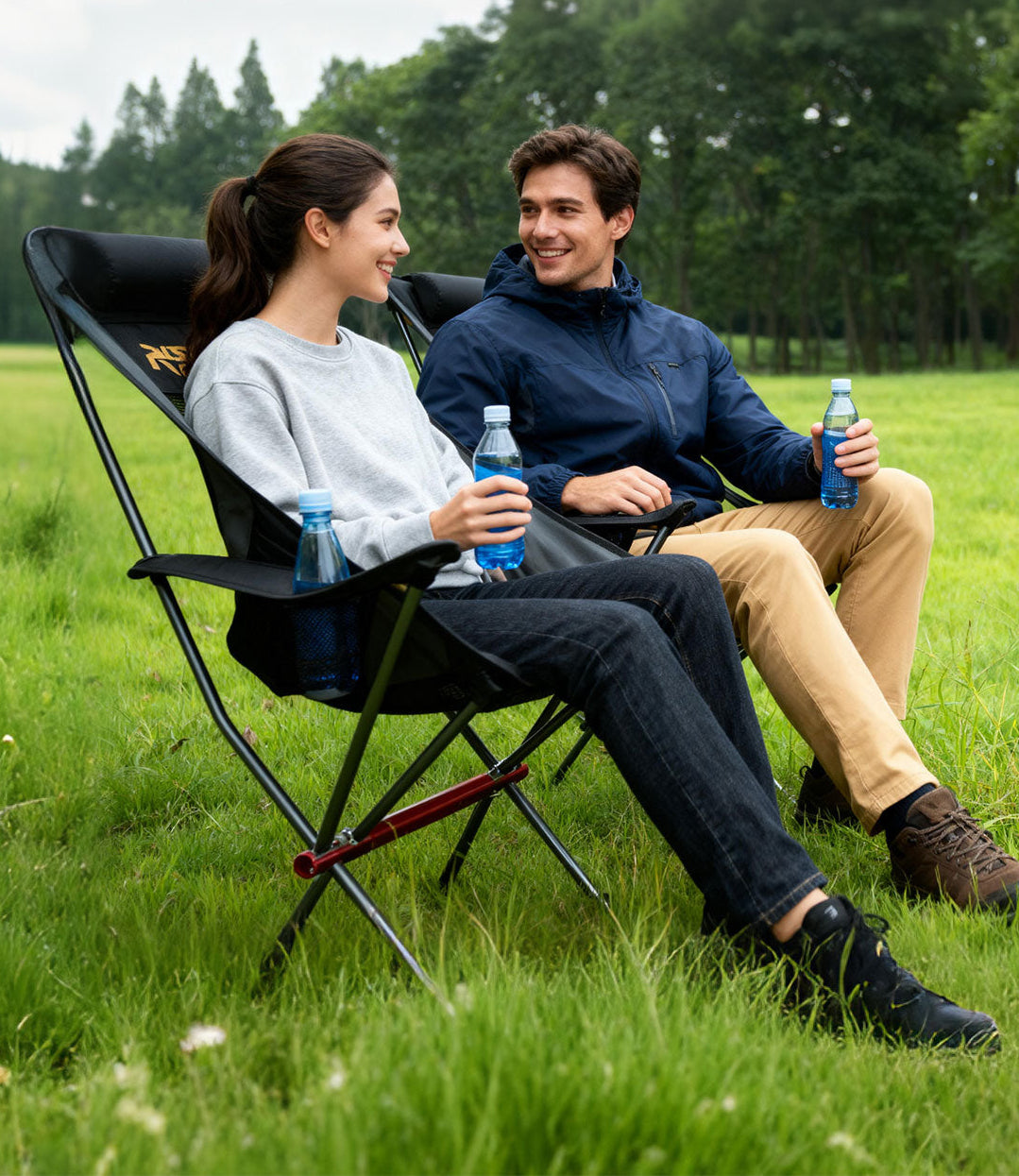 Couple sitting in RoosCamp High-Back Camping Armchairs in a meadow with forest backdrop